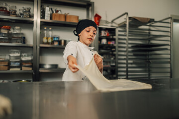 Child chef working with dough on a shiny metal table in the kitchen