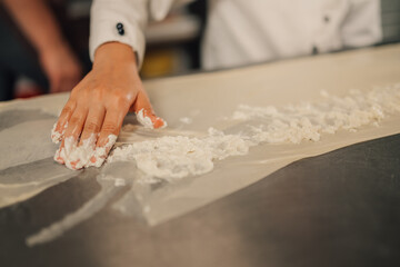 Hand spreading creamy filling on dough sheet in a kitchen setting