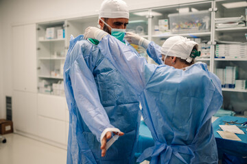 Medical team assisting each other with sterile gowns for surgery.