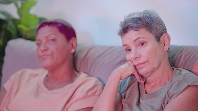 Aged same sex gay couple watching boring tv show together sitting on couch in their living room. Elderly gay couple
