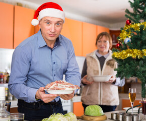 Man with plate of meat during cooking for xmas dinner, senior woman behind