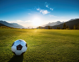 Soccer ball on green grass field with high mountains in the background