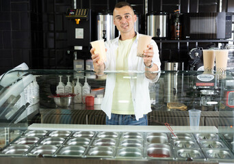 Friendly seller standing behind glass counter with large selection of flavorful colorful fruit...