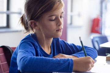 In school, boy writing with pencil in classroom, concentrating on task