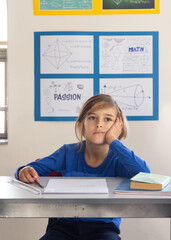 In school, boy sitting at desk daydreaming with books and papers
