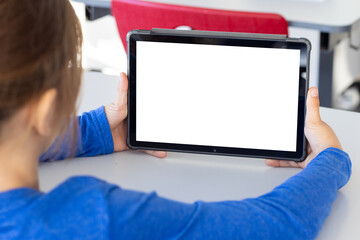 Holding tablet with blank screen, boy sitting at school desk, copy space