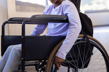 Sitting in wheelchair, african american girl in school hallway wearing purple shirt