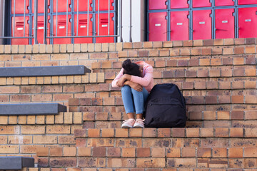 Sitting on school steps, african american girl with backpack feeling sad and alone