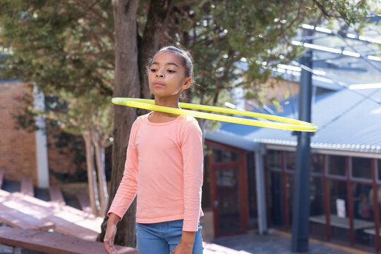 Hula hooping, african american girl in schoolyard enjoying outdoor activity during break - Powered by Adobe