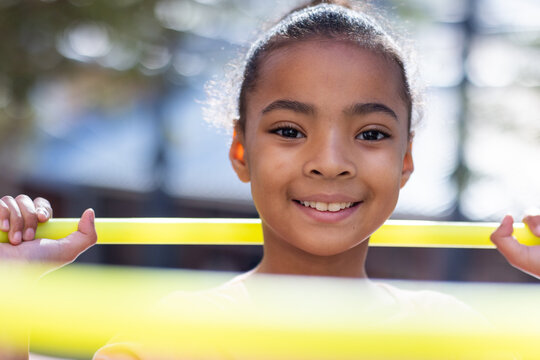 Smiling african american girl holding yellow hula hoop, enjoying outdoor school activity - Powered by Adobe