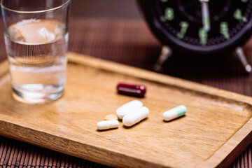 Assorted pills with water and vintage alarm clock on tray