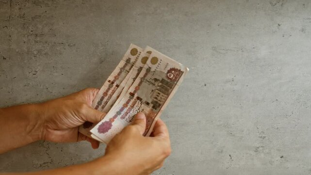 Hands holding egyptian pounds against a concrete background, depicting a financial theme in egypt with a focus on handling money and finance