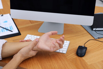 Man suffering from pain in wrist while working on computer at wooden table, closeup. Carpal tunnel...