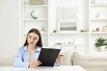 Budget planning. Beautiful young woman with papers at white table indoors