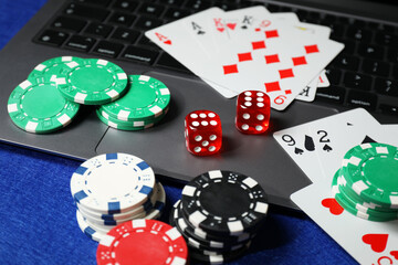 Poker chips, laptop, playing cards and dices on blue table. Online game