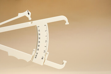 Plastic body fat caliper on beige background, closeup. Space for text