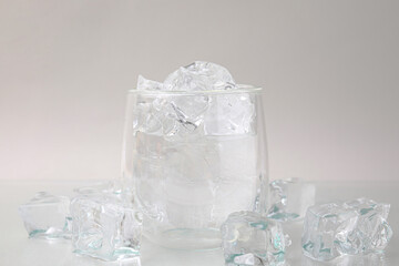 Refreshing water in glass with ice cubes on light background