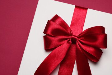 Gift box with red bow on burgundy background, above view