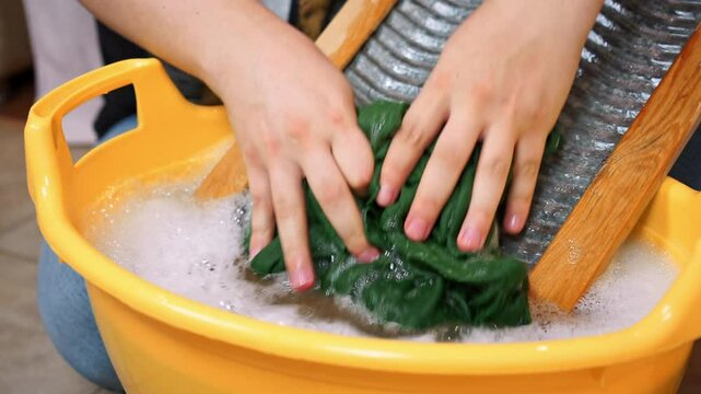Close-up of clothes being scrubbed on a washboard in a yellow basin. captures traditional laundry methods and sustainability themes.