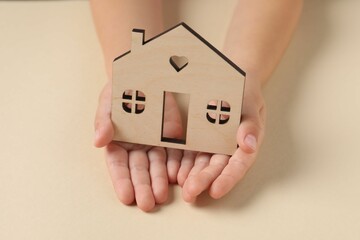 Adoption concept. Kid with cutout of house at beige table, closeup