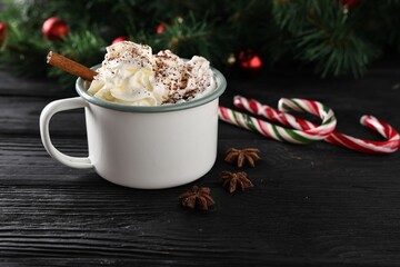 Tasty hot cocoa drink with whipped cream in mug and spices on black wooden table
