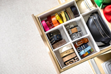 A drawer in a wardrobe with fashionable belts and accessories neatly arranged. Concept of storage
