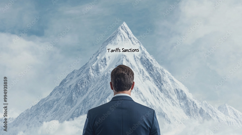 Wall mural a man in a suit is looking up at a mountain. the mountain is covered in snow and the sky is cloudy. 