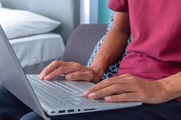 Naklejka premium Man working on laptop in his bedroom. Working from home, working on holiday or working from anywhere concept.
