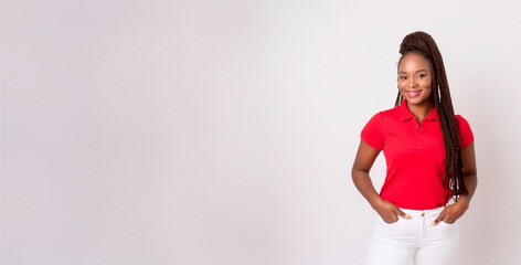 A portrait of a Black woman wearing a red polo shirt and white skinny pants against a background of white walls.