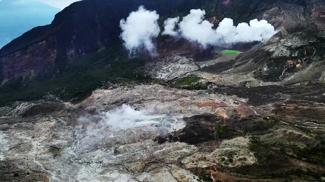 Stunning aerial footage of Mount Papandayan's volcanic crater, showcasing its majestic presence amidst lush mountains and ethereal cloud cover. This dramatic landscape in Indonesia