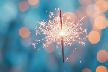 A brightly lit sparkler in the foreground, casting a warm glow, with light blue background