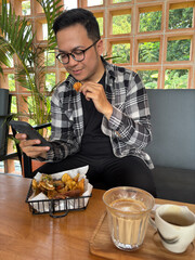 Man sitting in cafe looking at smartphone while eating snacks