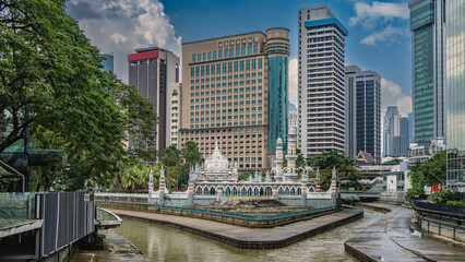 Obraz premium The urban landscape of Kuala Lumpur. The oldest mosque Masjid Sultan Abdul Samad is at the confluence of two rivers. Arches, minarets, domes against the modern skyscrapers. Lush tropical vegetation