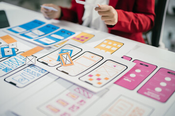 Web designer is reviewing mobile application wireframes at their desk, deciding which design...