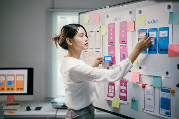 Young asian woman working as ux ui designer is designing a mobile application, using sticky notes...