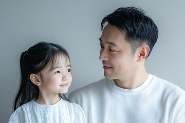 Young Chinese father and cute daughter interacting and smiling in plain background, dressed in simple Uniqlo clothes, family photo portrait.
