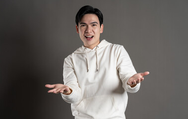 Portrait of Asian man wearing hoodie and posing on gray background.