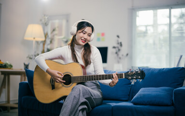 Young woman playing acoustic guitar in her cozy living room, fully immersed in music, showcasing...