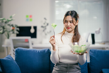 Young businesswoman looks disgusted while eating salad in her home office, showing her commitment...