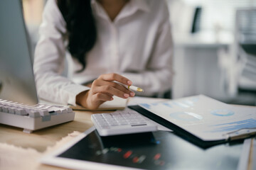 Focused businesswoman reviewing financial data on computer at office desk, surrounded by technology and paperwork, strategizing for success