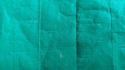 A close-up shot of a green fabric with creases and folds. The fabric has a textured appearance and a slightly faded color. It could be used for backgrounds, textures, or design elements.