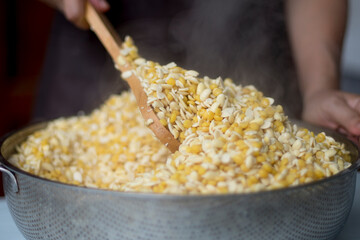 A person use wooden ladle stir boiled chickpeas and soy bean in stainless steel sieve for reduce temperature closed up selective focus and blur background. Prepared to making tempeh or tempe.