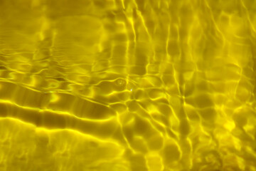Yellow water with ripples on the surface. Defocus blurred transparent gold colored clear calm water surface texture with splashes and bubbles. Water waves with shining pattern texture background.