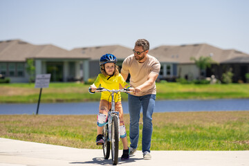 Fototapeta premium Happy Fathers day. Father teaching son riding bike. Father helping excited son to ride a bicycle in american neighborhood. Child in bike helmet learning to ride cycle with his dad. Fathers day.