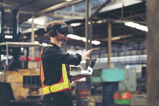 Male factory mechanic using virtual reality headset. Male engineer working with virtual reality headset and holding laptop computer in industry factory while control machinery