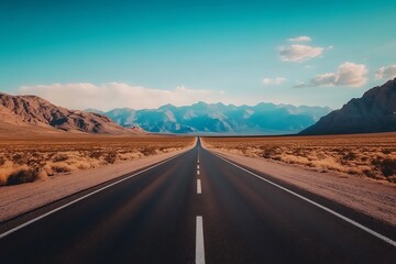 Long straight country road with great mountains in horizon and clear blue sky above