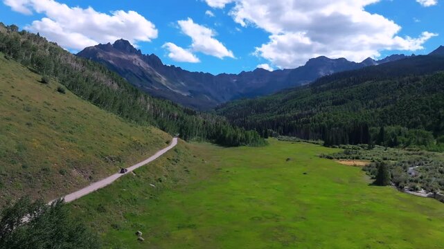 Subaru driving Mount Sneffels Wilderness Blue Lakes Trailhead Last Dollar Road Ridgway Colorado aerial drone summer green lush Uncompahgre National Forest Aspen trees blue skies clouds forwards