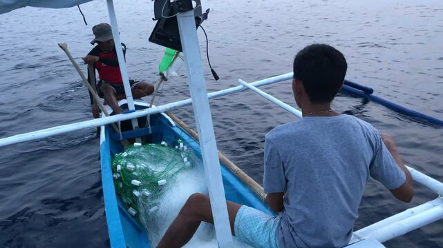 fishermen are spreading a mile-long nylon fishing net into the depths of the sea while aboard a wooden boat