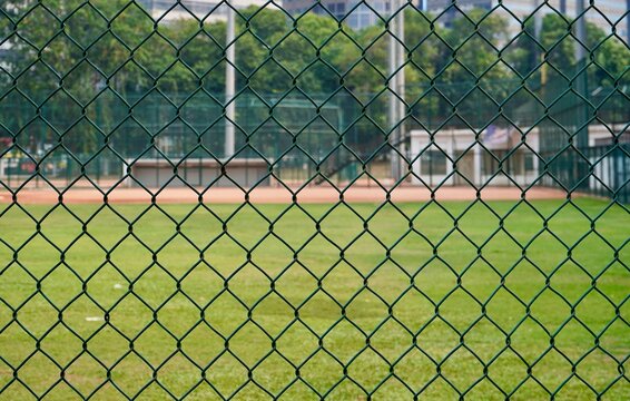 Green metal net chain link baseball field fence barrier isolated on horizontal green grass environment background.