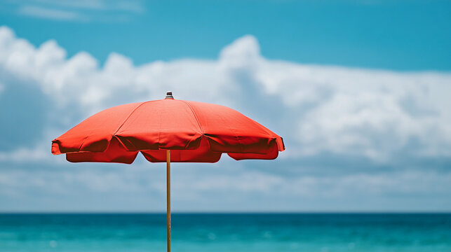 A vibrant red beach umbrella stands against a clear blue sky by the ocean in summer